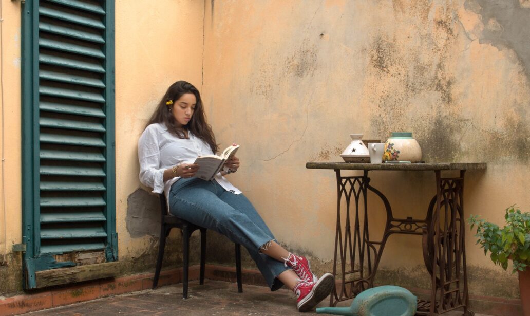 Kobieta siedzi na krześle przed domem i czyta książkę
